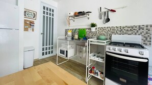 Eine kompakte Küche mit Herd, Mikrowelle und verschiedenen Küchenutensilien an der Wand.
