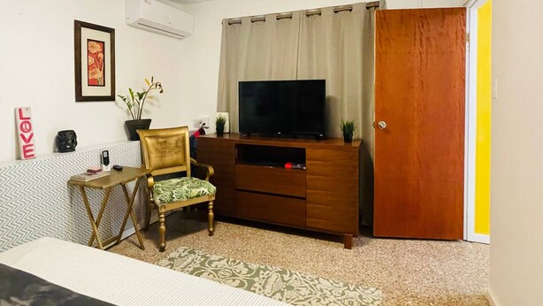 Une petite pièce meublée, comprenant un meuble de rangement en bois, un téléviseur, une chaise, une petite table et une porte.