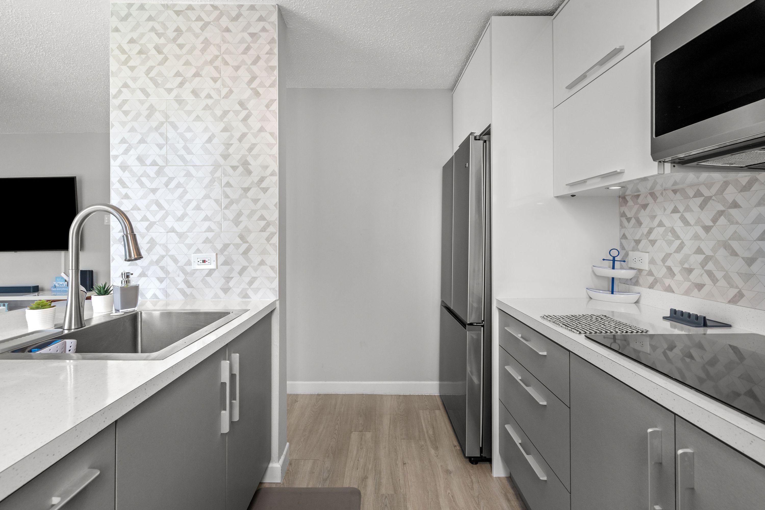 A modern kitchen with a stainless steel refrigerator, built-in oven, and a flat-screen TV mounted above the counter.