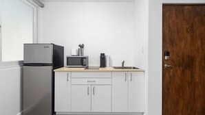 A compact kitchen with white cabinets, a stainless steel refrigerator, a microwave, and a coffee maker. - 101condado65avenue-bl (San Juan)