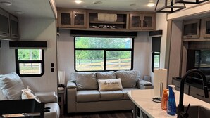 Interior d'una caravana compacta amb petita cuina, zona de seients amb finestra i taula de dinar.