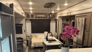 Cuina d'autocaravana compacte amb una illa central, un refrigerador i una zona de dinar.