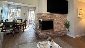 A living room with a fireplace, a dining area with a table and chairs, and a TV mounted on the wall.