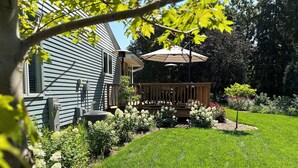 A backyard with a wooden deck, a patio umbrella, and a variety of plants and flowers.