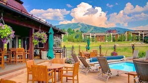 A patio with wooden furniture and a pool, overlooking a mountain range. - Luxurious 4-bedroom home in Steamboat Springs with stunning Flat Tops views. (Steamboat Springs)