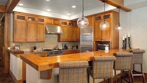 A kitchen with wooden cabinets, a stainless steel refrigerator, a central island with bar stools, and pendant lighting. - Luxurious 4-bedroom home in Steamboat Springs with stunning Flat Tops views. (Steamboat Springs)