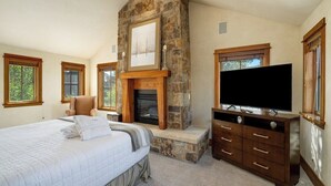 A bedroom with a stone fireplace, a large bed, a TV, and a dresser. - Luxurious 4-bedroom home in Steamboat Springs with stunning Flat Tops views. (Steamboat Springs)