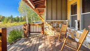 A wooden deck with rocking chairs and a stone wall. - Luxurious 4-bedroom home in Steamboat Springs with stunning Flat Tops views. (Steamboat Springs)