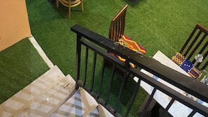 Un restaurant situé sur le toit, avec une terrasse extérieure aménagée avec du gazon synthétique, comprenant des tables et des chaises, un escalier et une rambarde.