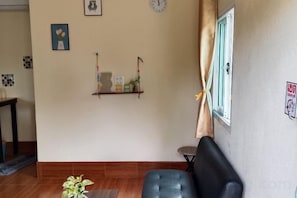 Un salon comprenant un canapé, une petite table, une plante en pot et une étagère ornée d’objets décoratifs.