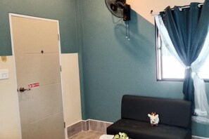 A room with a bed, a small table, a sofa, a fan, a window with curtains, and a door. - Rim nam Resort (Nong Khai)