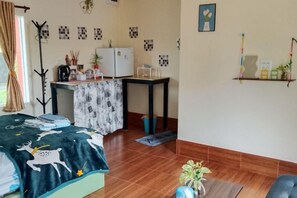 A room with a bed, a desk, a chair, a refrigerator, and a shelf with items. - Rim nam Resort (Nong Khai)