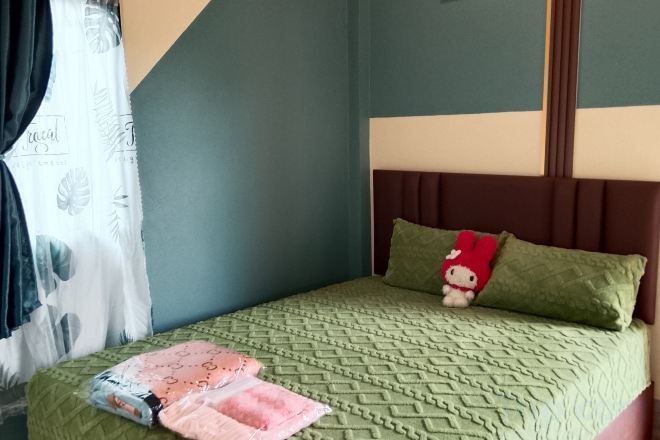 A bed with a patterned bedspread, a pillow with a Hello Kitty design, and a headboard.