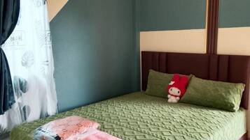 A bed with a patterned bedspread, a pillow with a Hello Kitty design, and a headboard.