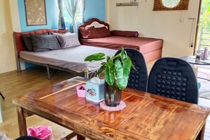 A room with a bed, a table with a vase of plants, and a chair. - Rim nam Resort (Nong Khai)