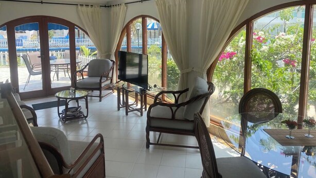 Amplia sala de estar con televisión, asientos cómodos y ventanas grandes con vistas al exterior.