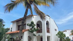 Un edificio blanco con techo de tejas rojas, varios balcones y una palmera en primer plano.