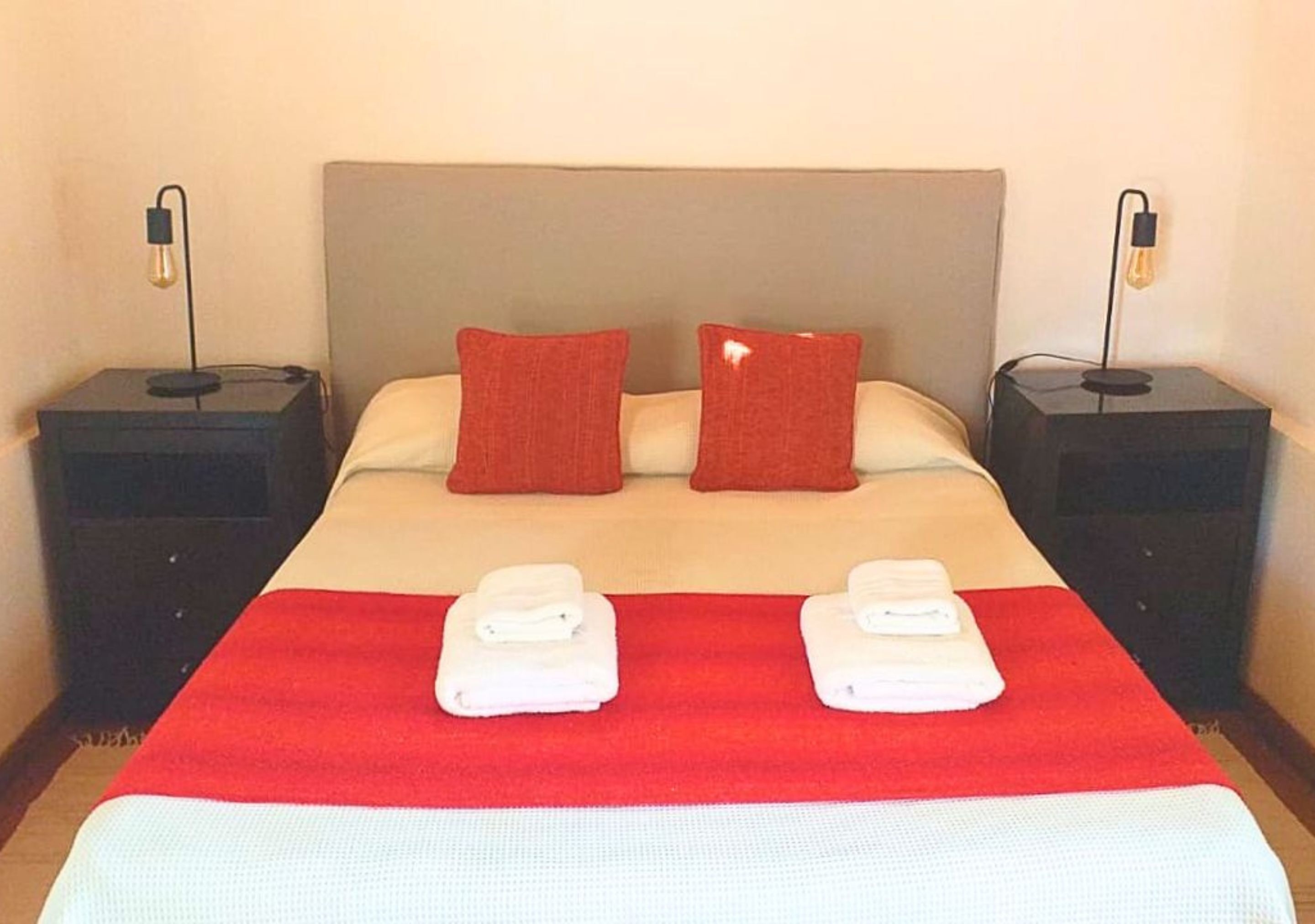 Una cama bien hecha con una colcha roja, dos almohadas y dos toallas dobladas sobre la cama.