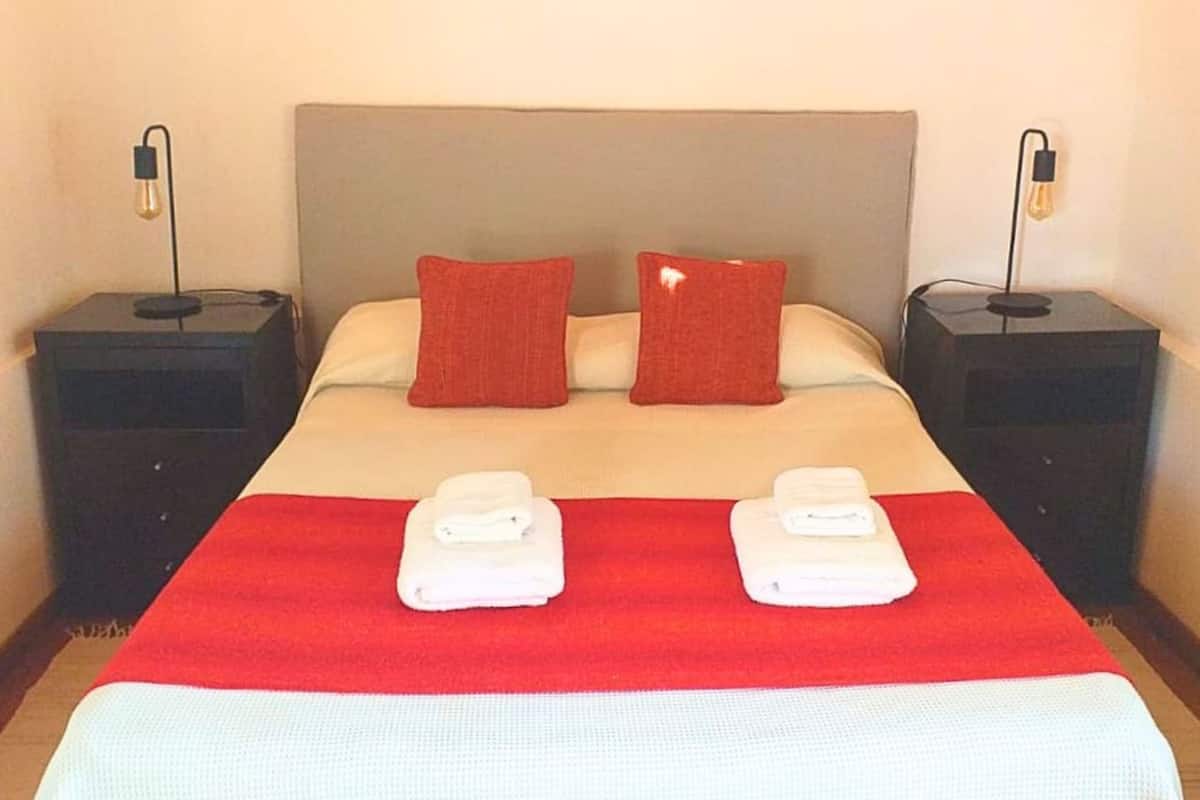 Una cama bien hecha con una colcha roja, dos almohadas y dos toallas dobladas sobre la cama.