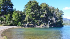 A natural landscape with a clear lake, sandy beach, and dense forested area.