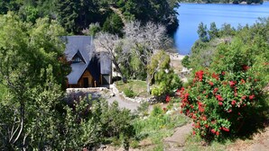 A cabin with a metal roof, surrounded by dense greenery and a lake.