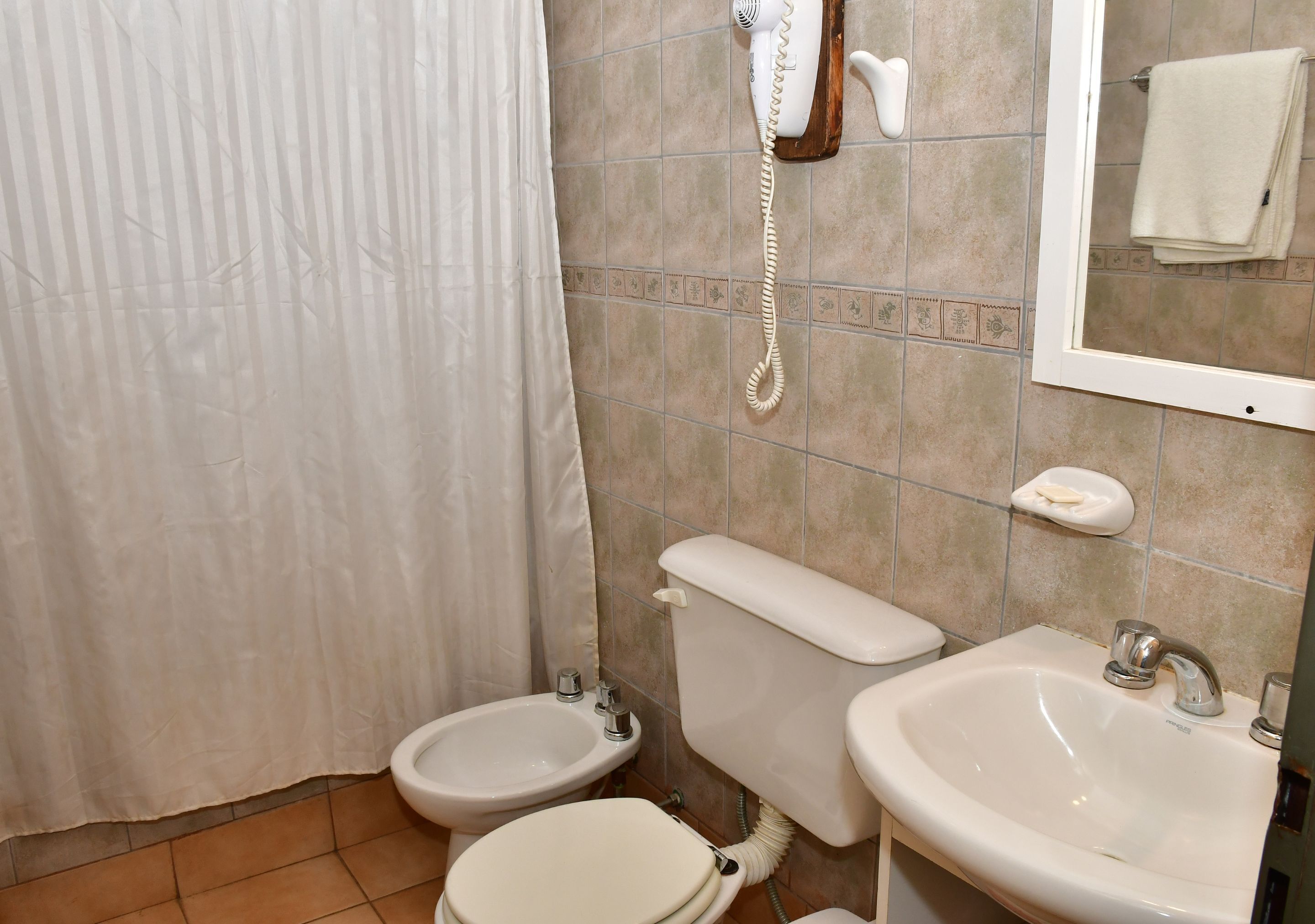 Un bagno con toilette, bidet, lavandino e un telefono fissato alla parete.