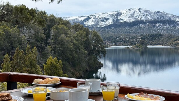 A breakfast table with various dishes and drinks, overlooking a lake and mountains.