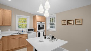 A modern kitchen with wooden cabinets, white countertops, a central island, and pendant lighting. - Charming 3BR/2BA Sleeps 6 in Graham, NC has everything you need! (Graham)