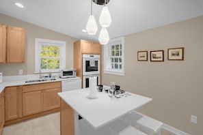 A modern kitchen with wooden cabinets, white countertops, a central island, and pendant lighting. - Charming 3BR/2BA Sleeps 6 in Graham, NC has everything you need! (Graham)