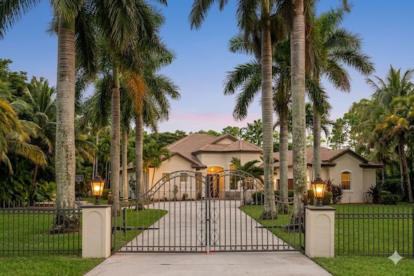 A gated residential property with a house, surrounded by palm trees and a well-maintained lawn.