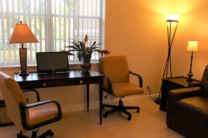 A room with a desk, two chairs, a laptop, a vase with flowers, and two floor lamps.