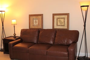 A brown leather sofa in a room with two framed artworks on the wall and two floor lamps.