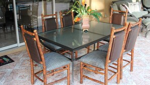Una mesa de comedor con cubierta de vidrio rodeada de seis sillas de madera con asientos acolchados. Un jarrón con flores está sobre la mesa.