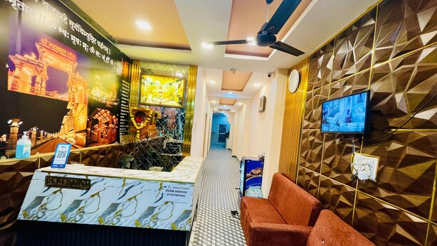 A reception area with a reception desk, a sofa, a television, and a patterned wall. - Hotel Jay Shree (Ujjain)