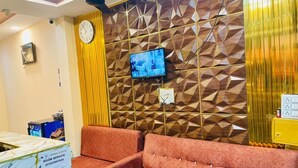 A reception area with a sofa, a clock, a television, and a desk with a sign indicating room service. - Hotel Jay Shree (Ujjain)