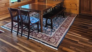 A wooden cabin interior with a dining table, chairs, a rug, and a hanging light fixture. -  Beautiful 5-bedroom log cabin with spectacular mountain views. (Newland)