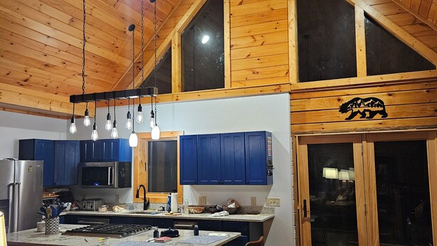 A spacious kitchen with wooden ceiling and cabinets, a large island with bar stools, and a dining area with a red rug. -  Beautiful 5-bedroom log cabin with spectacular mountain views. (Newland)
