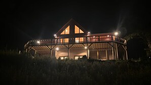 A large, two-story wooden building with a balcony and multiple windows, surrounded by tall grass. -  Beautiful 5-bedroom log cabin with spectacular mountain views. (Newland)