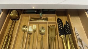 A drawer containing a set of gold-colored utensils including spoons, forks, and knives.
