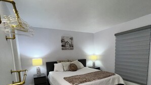 A bedroom with a bed, bedside tables, lamps, a picture on the wall, and a window with blinds.