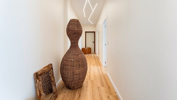 Un pasillo con una gran escultura tejida, suelo de madera y una lámpara moderna.