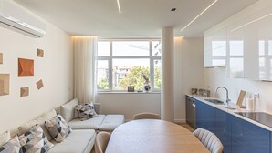 Una habitación moderna y bien iluminada con sofá, una mesa de comedor y una zona de cocina con lavaplatos y armarios.