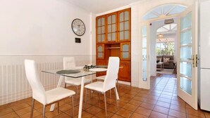 A dining area with a glass table and white chairs, a wooden cabinet, and a clock on the wall.