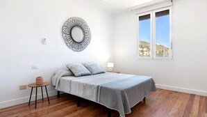 A bedroom with a bed, a round mirror, a small table, and a window with a view.