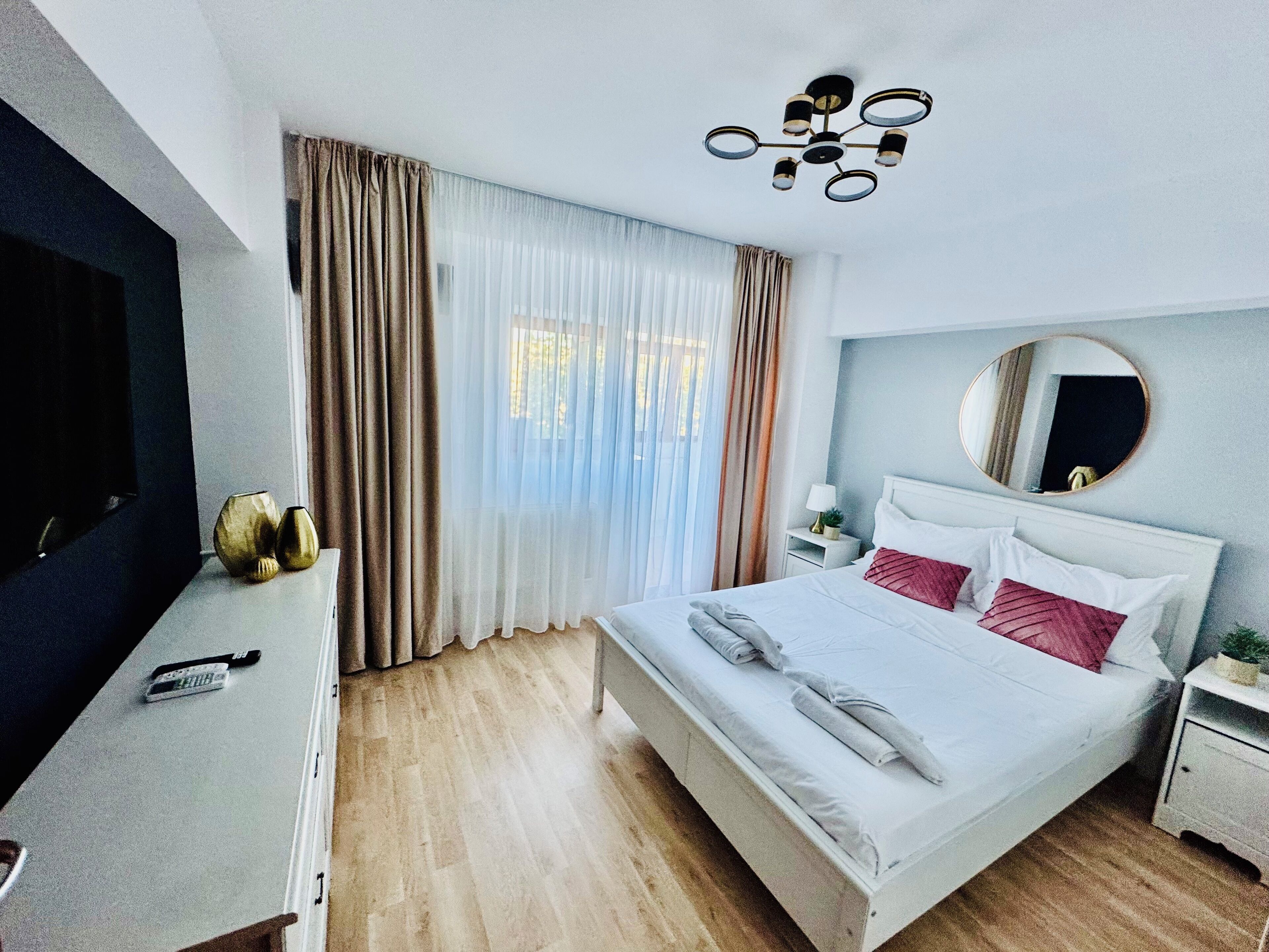 A hotel room with a bed, a TV, a bedside table, a mirror, and curtains.