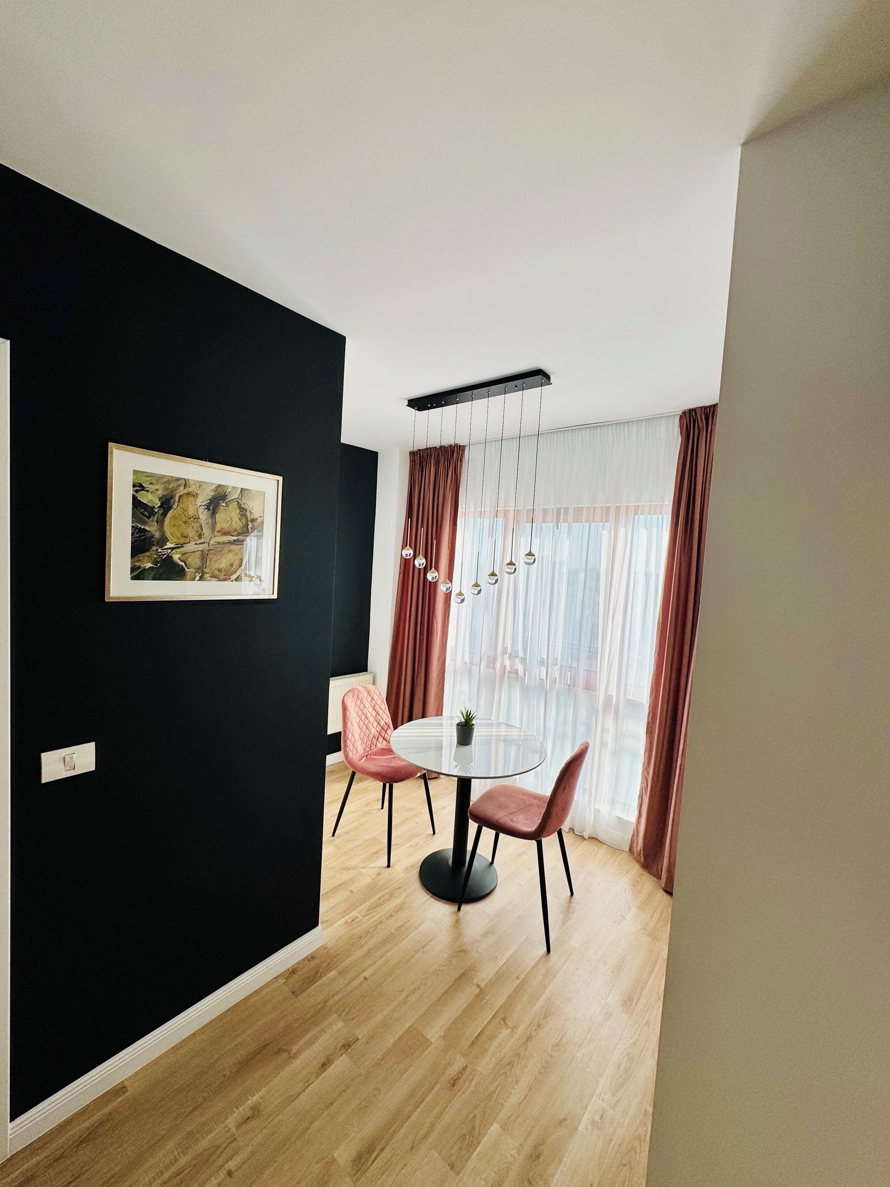 A modern dining area with a round table, two chairs, a hanging light fixture, and a painting on the wall.
