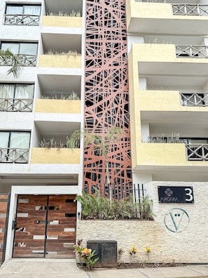 Un edificio moderno con una fachada distintiva, balcones con plantas y un letrero que indica el número 3.
