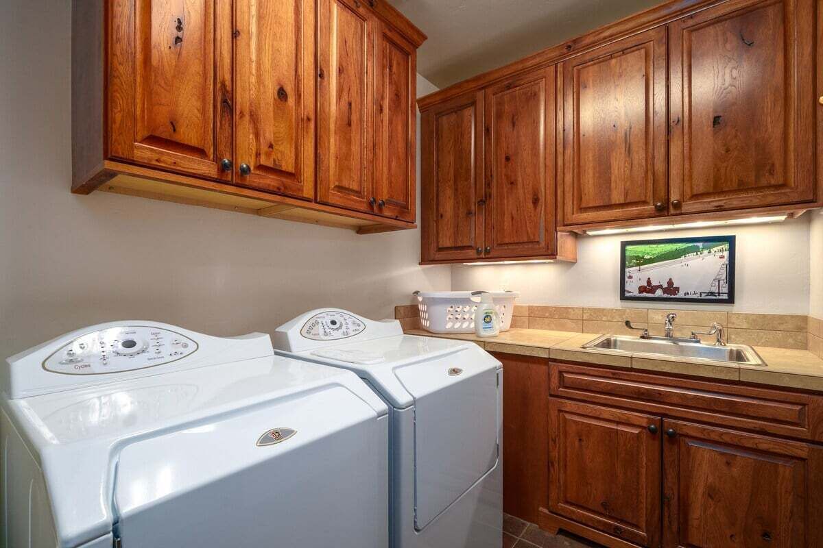 A kitchen with wooden cabinets, a washing machine, a sink, and a television mounted above the counter.