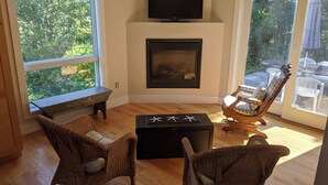 A living room with a fireplace, wicker furniture, and a TV mounted above it. - Knockout Truro Retreat with Sweeping Views, Modern Amenities, Walk to Beach (Truro)