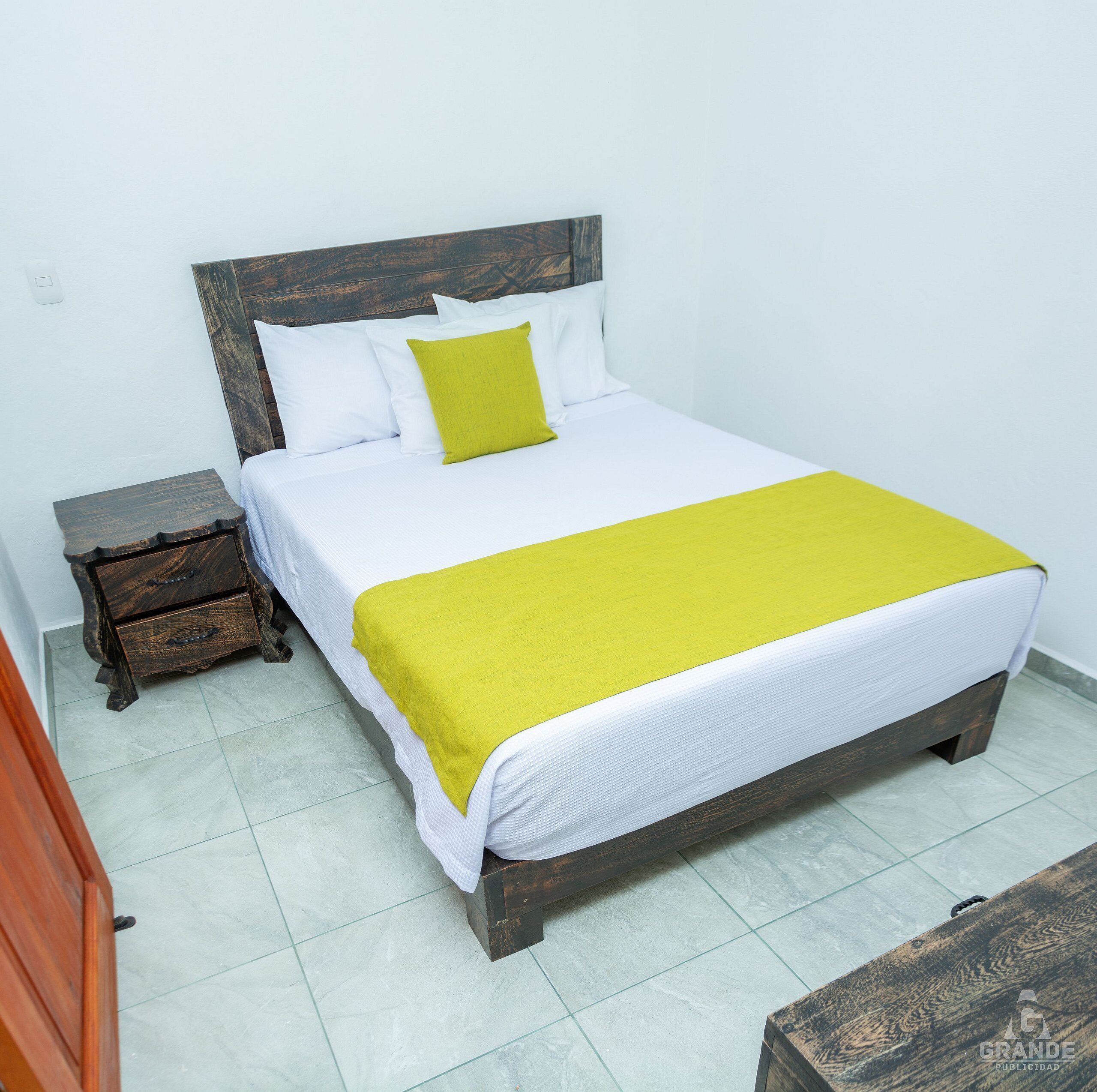 A bed with a wooden headboard, white bedding, and a yellow throw blanket.